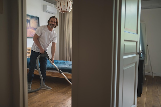 Photo man in white tshirt doing vacuum cleaning and looking involved