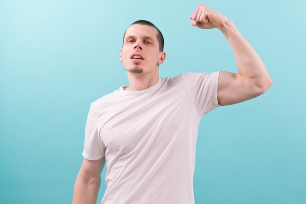 A man in a white tshirt shows his biceps on a blue background Confident Emotional Energy Hands Human Look Posing Power Sexual Cool Portrait