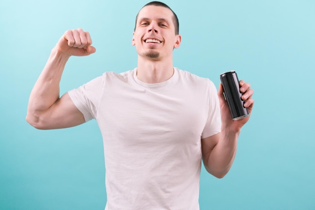 A man in a white tshirt smiles holds an empty black aluminum can and shows a biceps on a blue background cold liquid product mockup refresh refreshing storage brand energy