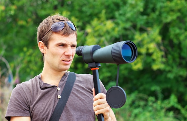 Man who is watching in spotting scope. Positive man looking through a telescope