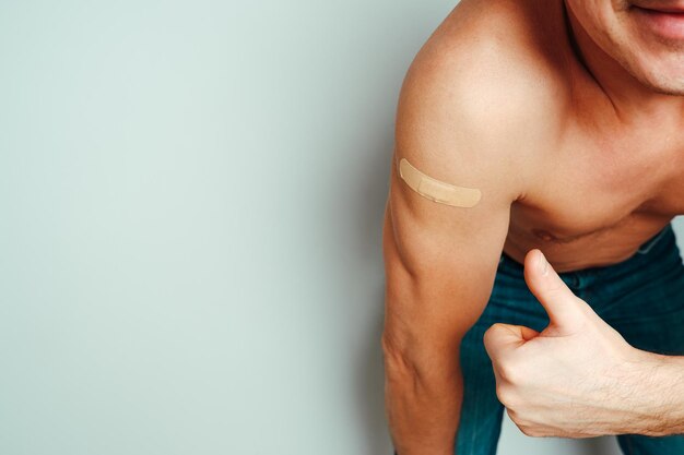 Foto un uomo che ha ricevuto un vaccino mostra la sua mano con un cerotto un uomo soddisfatto senza maglietta su uno sfondo chiaro si è chinato sulla telecamera e mostra una mano vaccinata