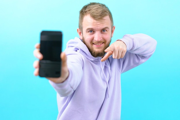 Man wijst met zijn wijsvinger naar de ongericht zwarte telefoon op een blauwe achtergrond Zelfverzekerd Emotie Facial Positief Online Student Touchscreen Trendy Aanbevelen Werk Adverteren Presentatie