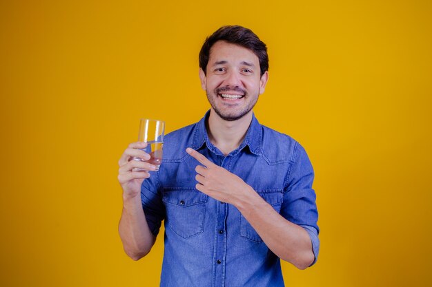 Man wijst naar het glas water in zijn hand op gele achtergrond. gezondheid en medisch concept