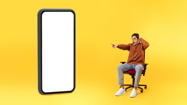 Man wijzende vinger opzij naar enorme telefoon scherm gele achtergrond