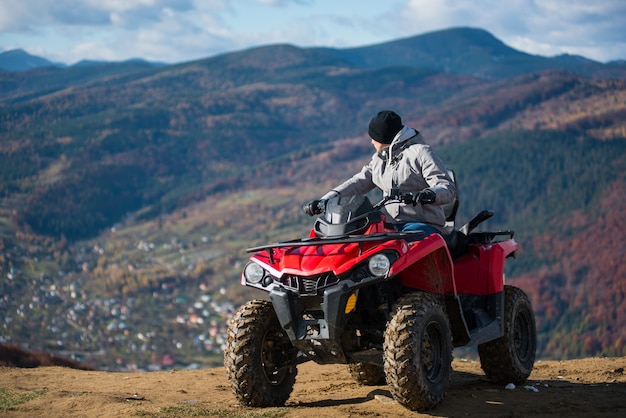 man in winter clothes on a red quad bike on a mountain top