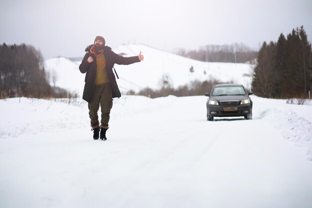 Photo a man in winter clothes on the street tourists travel through the snowy country on the way walk and hitchhike