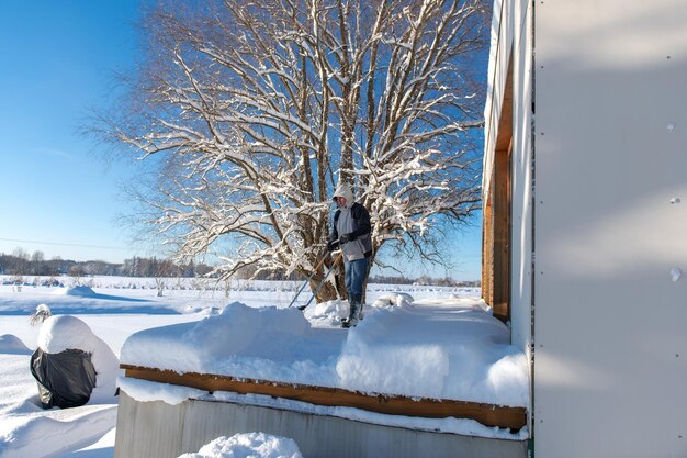 Foto un uomo in abiti da inverno con una pala per la neve che pulisce la neve dalla terrazza della casa