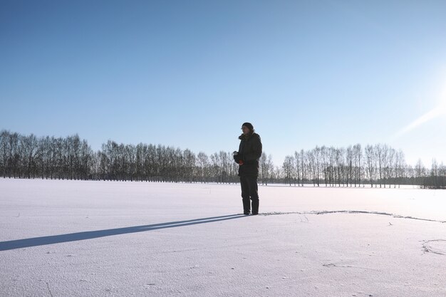 A man in the winter on the street. The guy walks on the winter road. A young man in a down jacket is jumping in the snow.