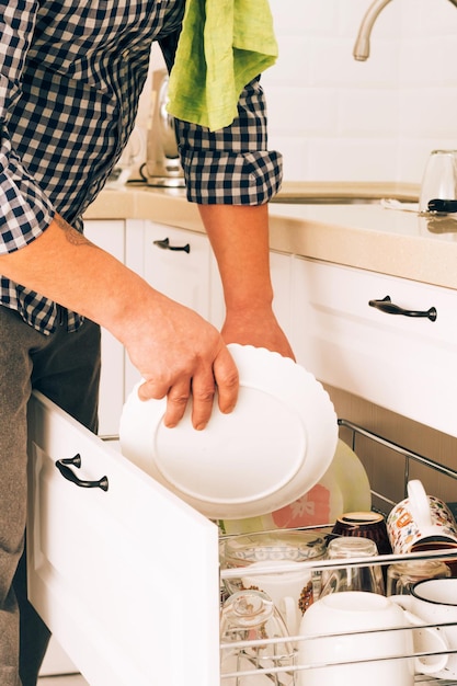 A man wipes clean dishes with a towel and puts them away to dry in the kitchen cabinet daily household chores