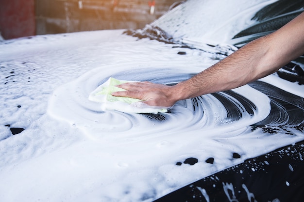 A man wipes the foam on the car with a rag. car wash