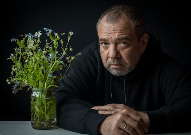 写真 家の暗い部屋で野花の花束を持った男