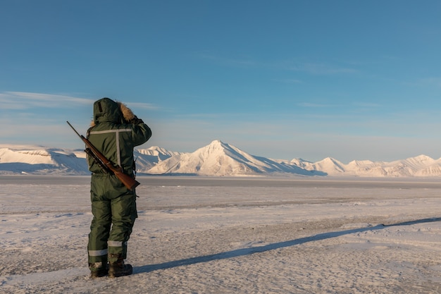 写真 スバールバルの北極の風景にライフルと双眼鏡を持った男