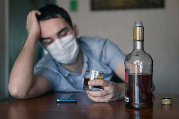 Man with alcohol Wearing Medical Mask. Drunkenness in conditions of self-isolation and quarantine. Treatment of coronavirus with alcohol. drunk, sad distraught, unemployed man. Corona Virus Concept