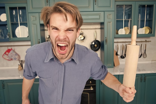 Man with angry face shout with rolling pin in kitchen