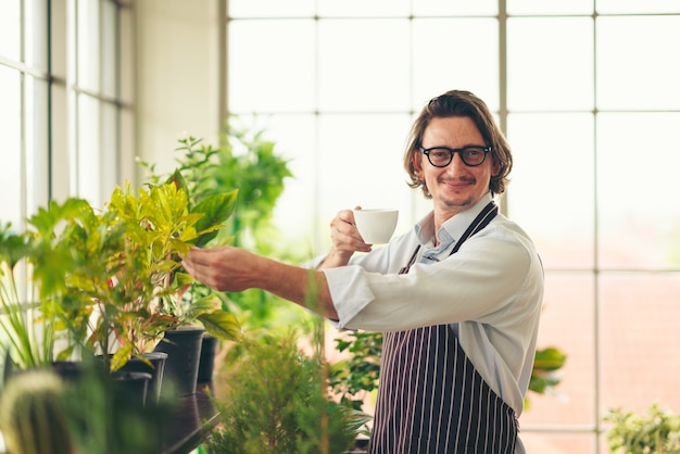 man with apron in greenhouse drinking coffee