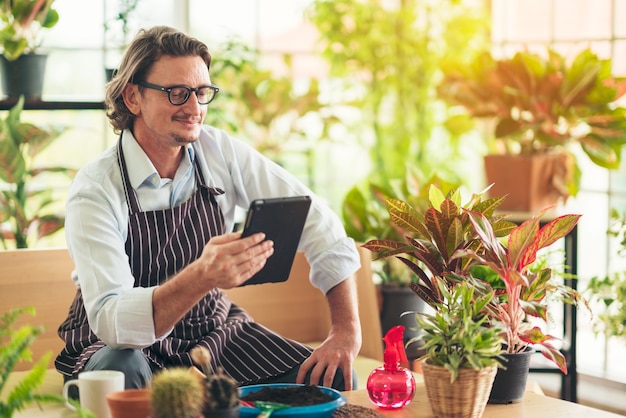 man with apron in greenhouse with tablet