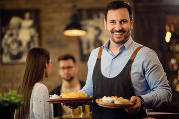 a man with an apron holding a tray of food with a woman in the background