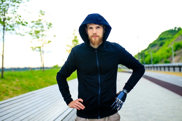 Man with arm prosthesis in sports clothing ready for morning workout outdoors Disabled sport concept