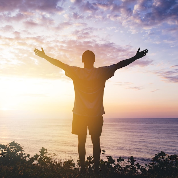 Man with arms outstretched celebrating in beautiful inspiring\
sunset