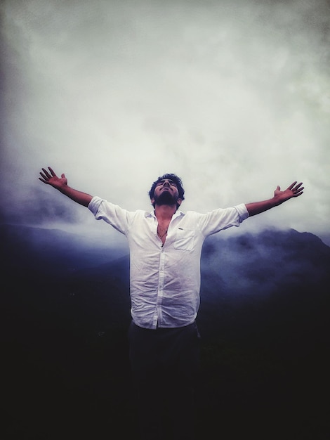 Foto uomo con le braccia tese in piedi contro il cielo nuvoloso