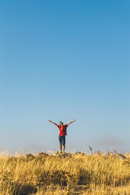 写真 腕を伸ばした男が晴れた空の前で野原に立っています