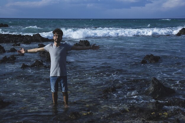 Foto uomo con le braccia tese in piedi sulla riva sulla spiaggia
