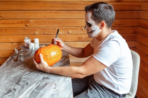 芸術的な不気味なメイクアップ立っている男は、カボチャを彫ってハロウィーンの準備をします