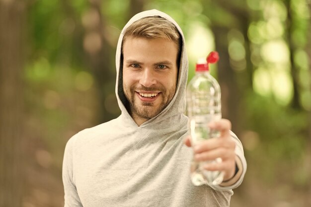 Man with athletic appearance holds bottle with water man\
athlete in sport clothes training outdoor sport and healthy\
lifestyle concept athlete drinks water after training nature\
background