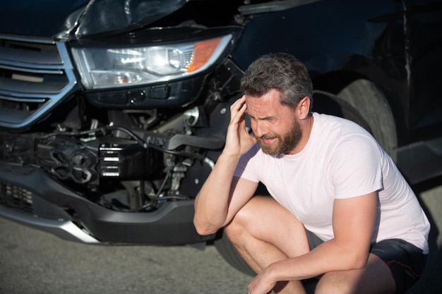 道路で壊れた自動車を持つ男。自動車保険。自動車事故。車両の衝突。係員の運転手はショックを受けました。ロードトリップの問題と支援。交通事故。交通事故後の悲しいドライバー。