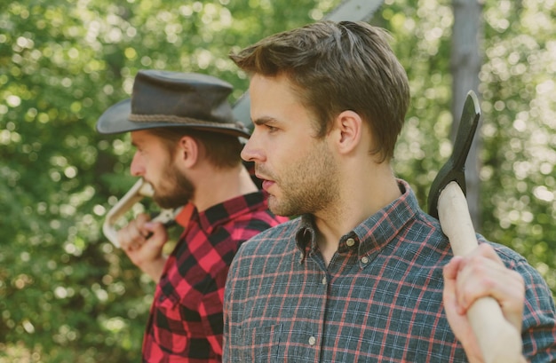 Photo man with axe in forest lumberjack woodcutter in a plaid shirt lumberjack brutal bearded man