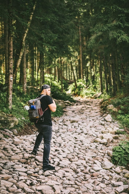 Man with backpack hiking in forest by stone path trail