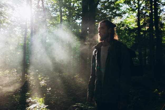 man with backpack standing in forest against trees