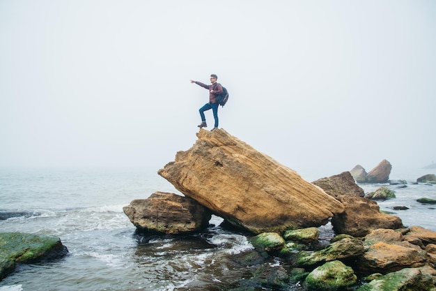 Man with a backpack stands on the edge of a cliff in the\
sea