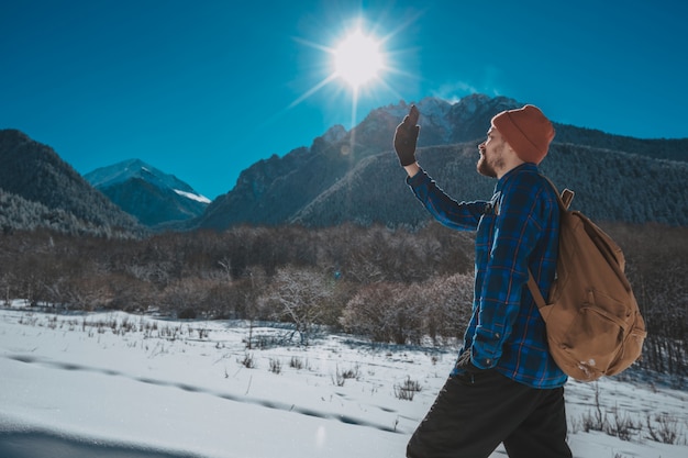 山でのトレッキングのバックパックを持つ男。寒さ、丘の上の雪。冬のハイキング。太陽と雪