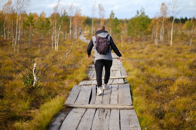 Photo a man with a backpack walks along a wooden path in a swamp in yelnya belarus