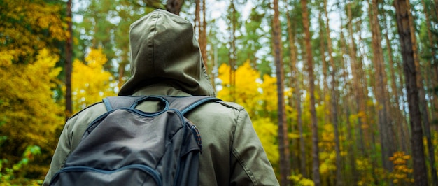 バックパックを持つ男は、素晴らしい秋の森を歩きます。