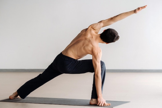 A man with a bare torso trains standing up, doing stretching in the gym.