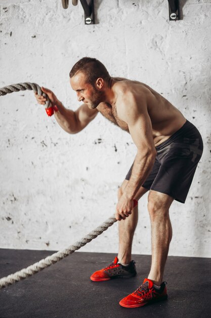 Man with battle ropes exercising in fitness gym