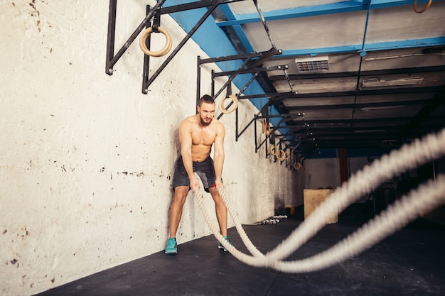 Uomo con le corde di battaglia che si esercitano nella palestra di forma fisica