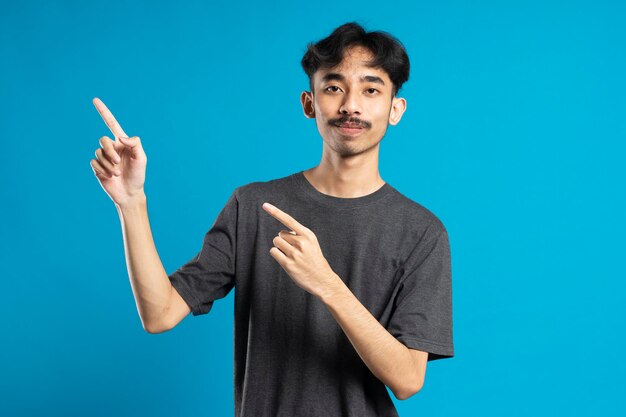 Man with beaming smile on blue background is pointing on empty copy space with his fingers