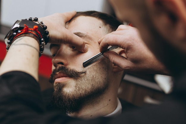 Photo man with a beard in a barbershop shaving and modeling a contemporary beard shape in retro style