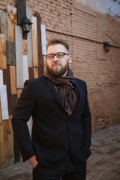 A man with a beard in a black warm coat with a scarf poses to advertise men's clothing in the winter. Advertise men's clothing