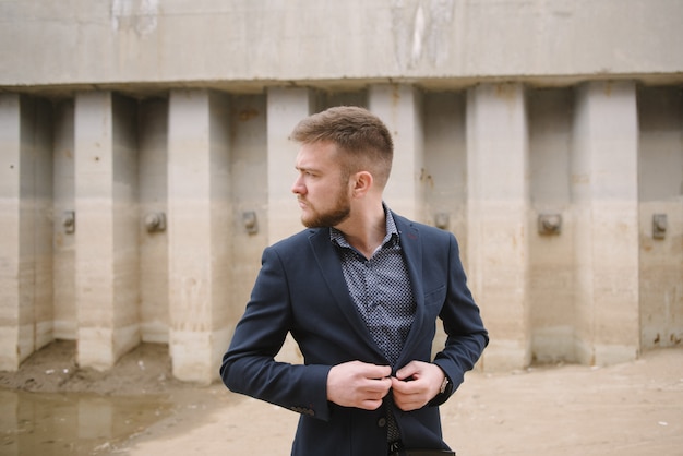 A man with a beard in a blue suit poses on the street to advertise men's clothing. 