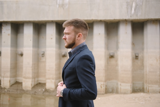 A man with a beard in a blue suit poses on the street to advertise men's clothing. 