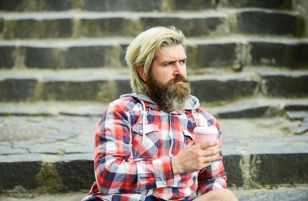 Photo man with beard drinking coffee hipster relax on stairs having rest caffeine dose pure pleasure good mood bearded man drink coffee urban background take away coffee third wave coffee culture