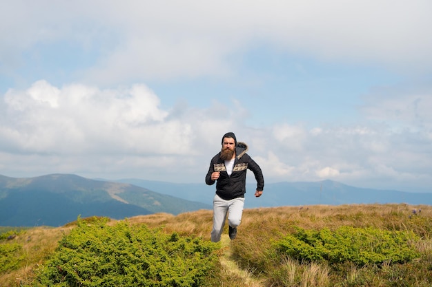 ひげを生やした男は山の上を自由に走りますヒップスターは空の背景をハイキングしながら自由に感じますヒップスターまたは残忍なマッチョは山を征服します残忍な外観の男はハイキング自由の概念