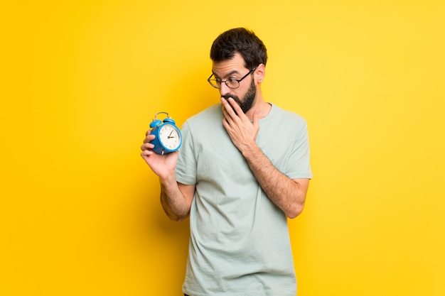 Man with beard and green shirt holding vintage alarm clock