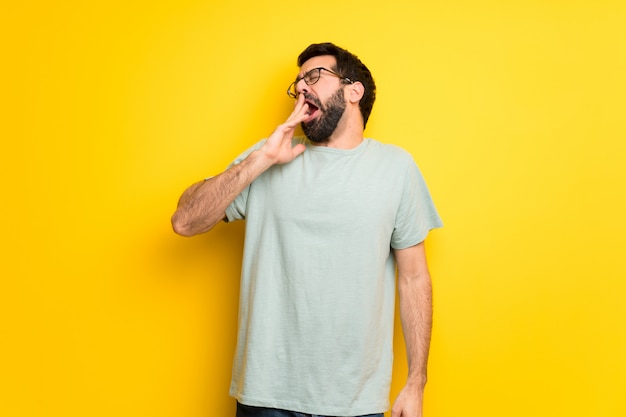 Man with beard and green shirt yawning and covering wide open mouth with hand