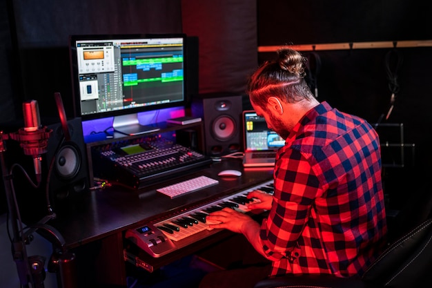 Photo man with beard in headphone is playing keyboard and singing his new song in stereo studio to record brand-new track