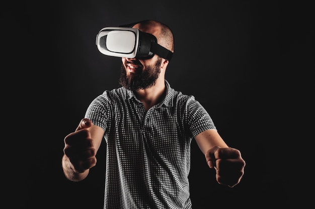 A man with a beard in the headset playing in virtual reality and smile Studio shot Black background